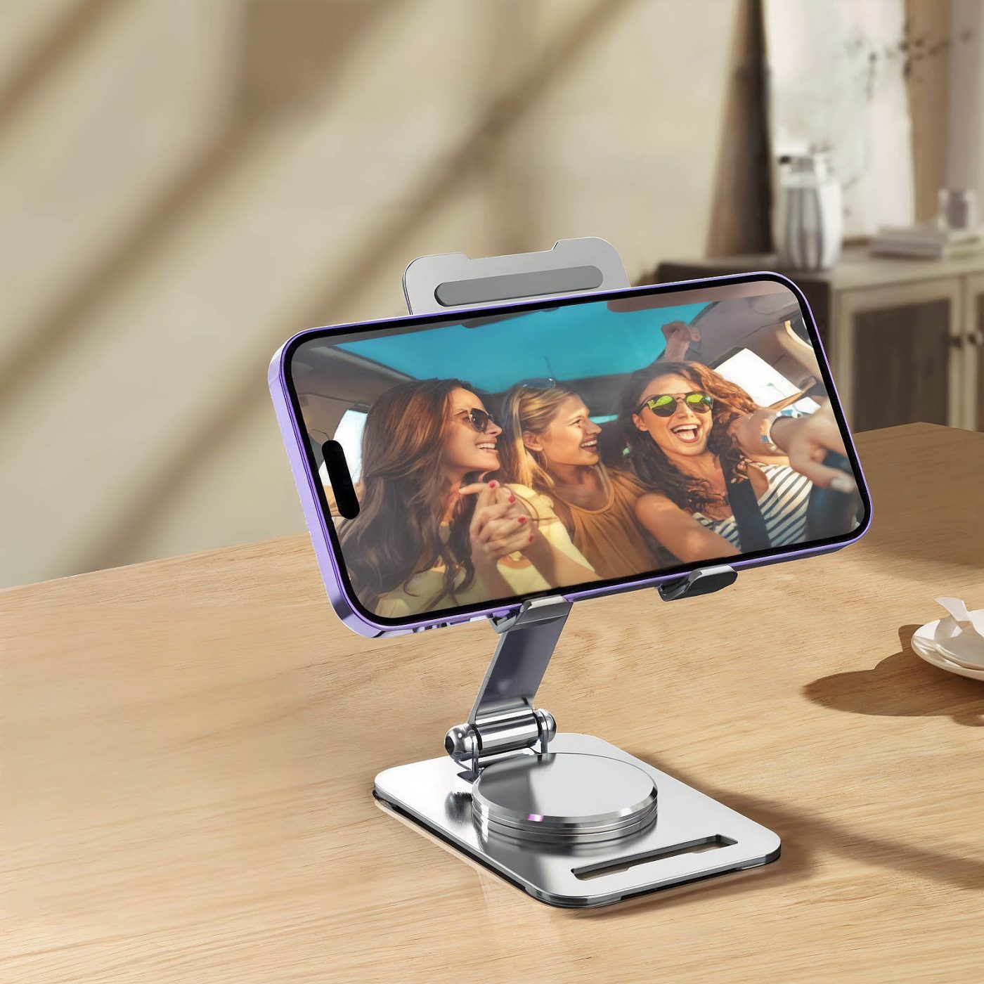 Silver stand holding a smartphone in landscape mode on a desk, playing a video of friends in a car