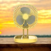Yellow folding fan fully extended placed outdoors with a sunset in the background