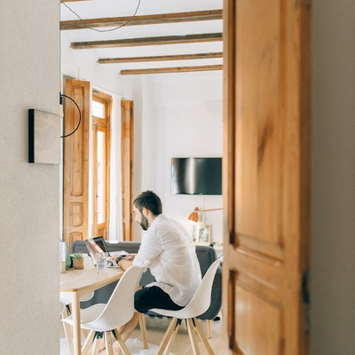 Man typing on a laptop at a dining table, with natural light filling room