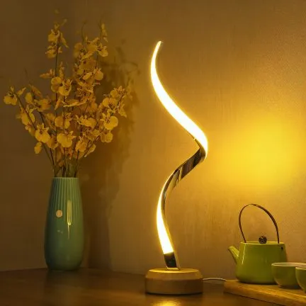 Curved LED table lamp glowing warm light on a wooden base, placed beside a vase and teapot on a table