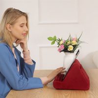 Woman at desk interacting with a tablet propped on burgundy red pillow stand cushion.