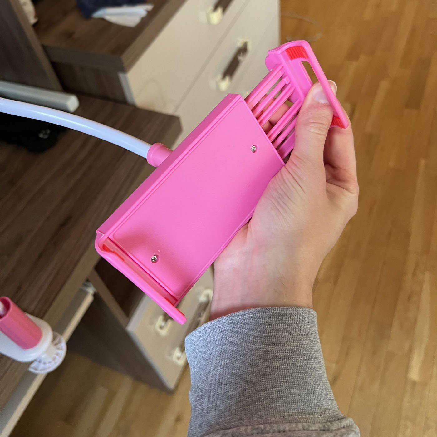 Hand stretching open the pink expanding grip of a gooseneck phone holder, demonstrating the spring mechanism.