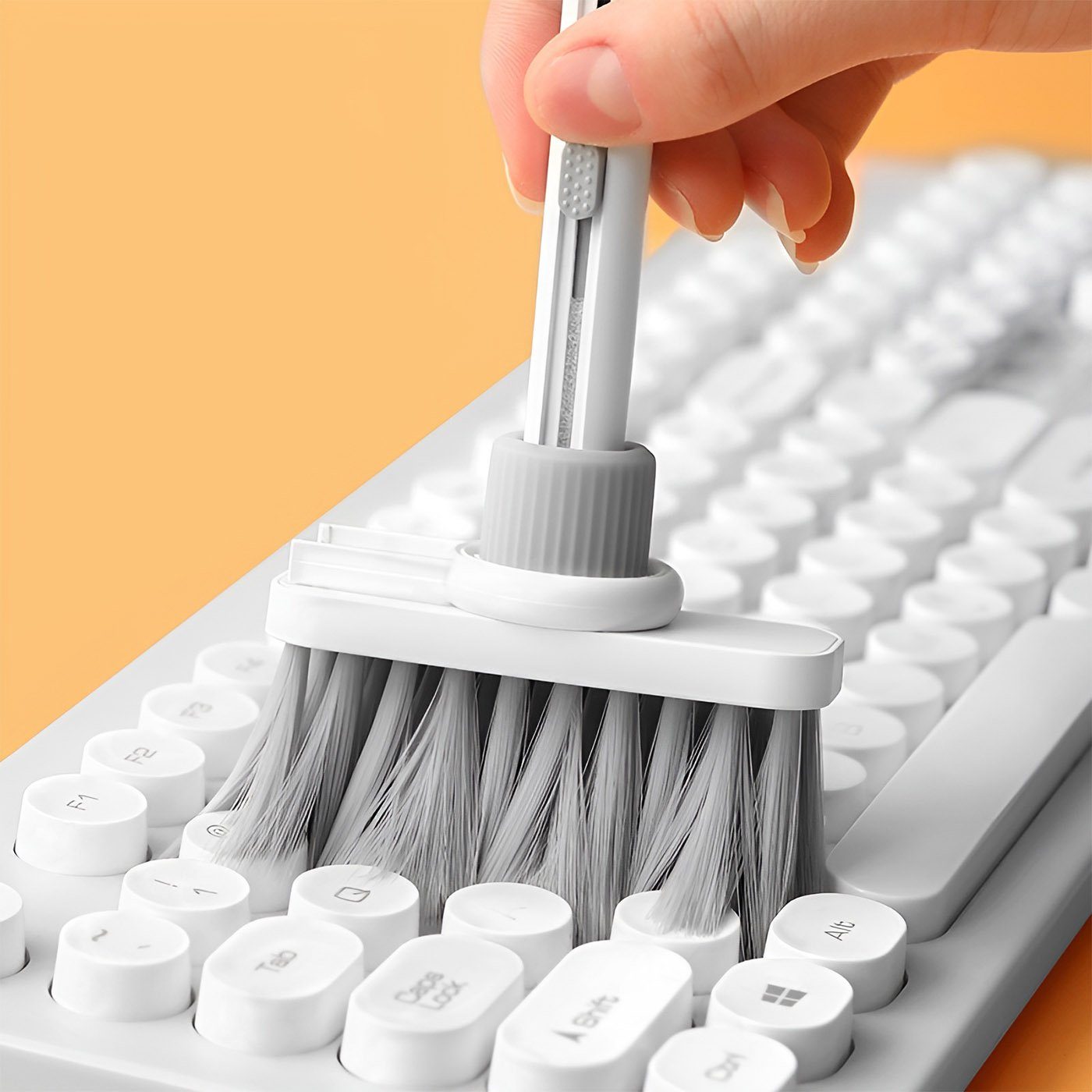 Hand using gray bristle keyboard brush to clean mechanical keyboard with rounded keycaps.