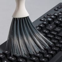 Close-up of soft, dense gray bristles cleaning dust and debris from a black computer keyboard.