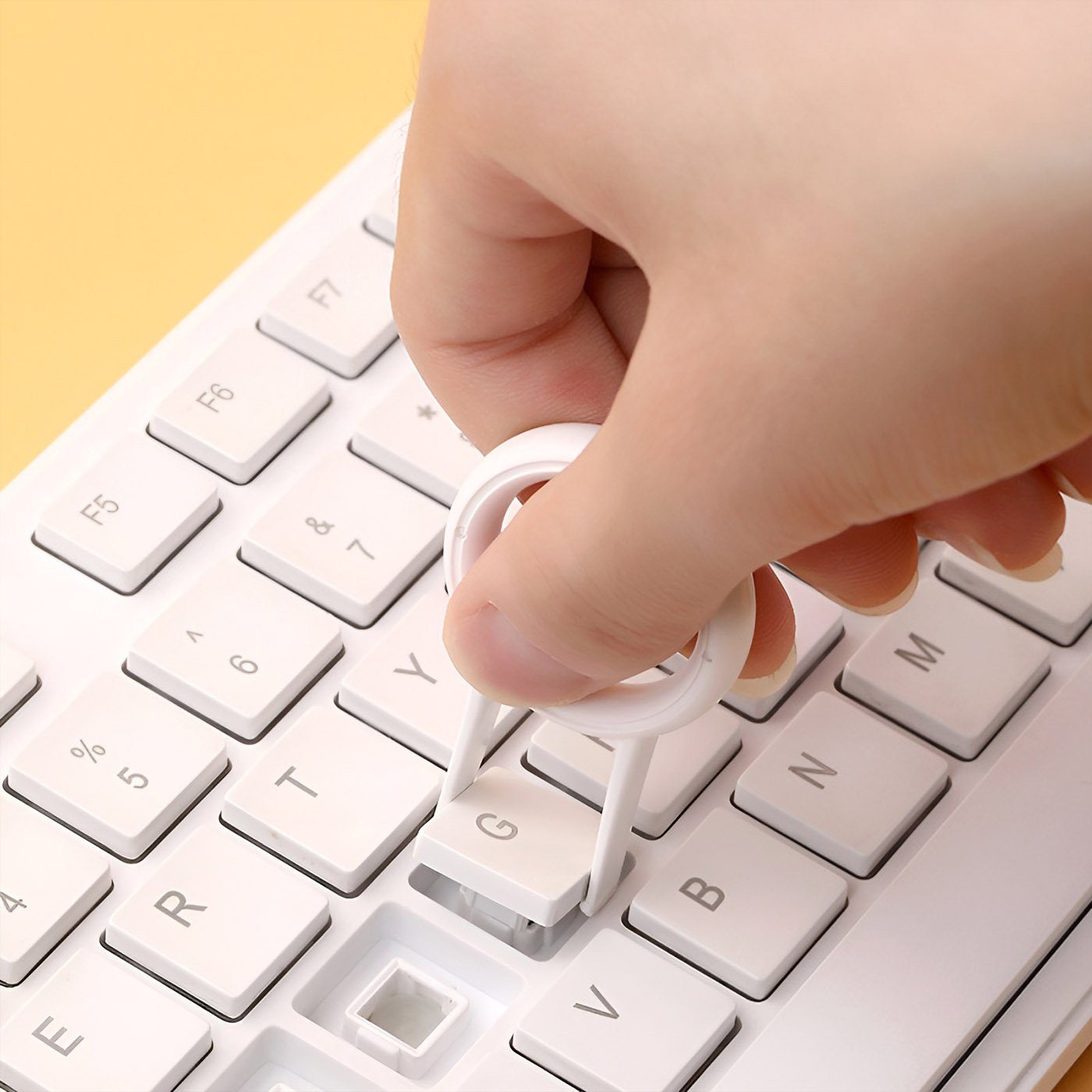 Hand using white plastic keycap puller tool to remove key from white mechanical keyboard.