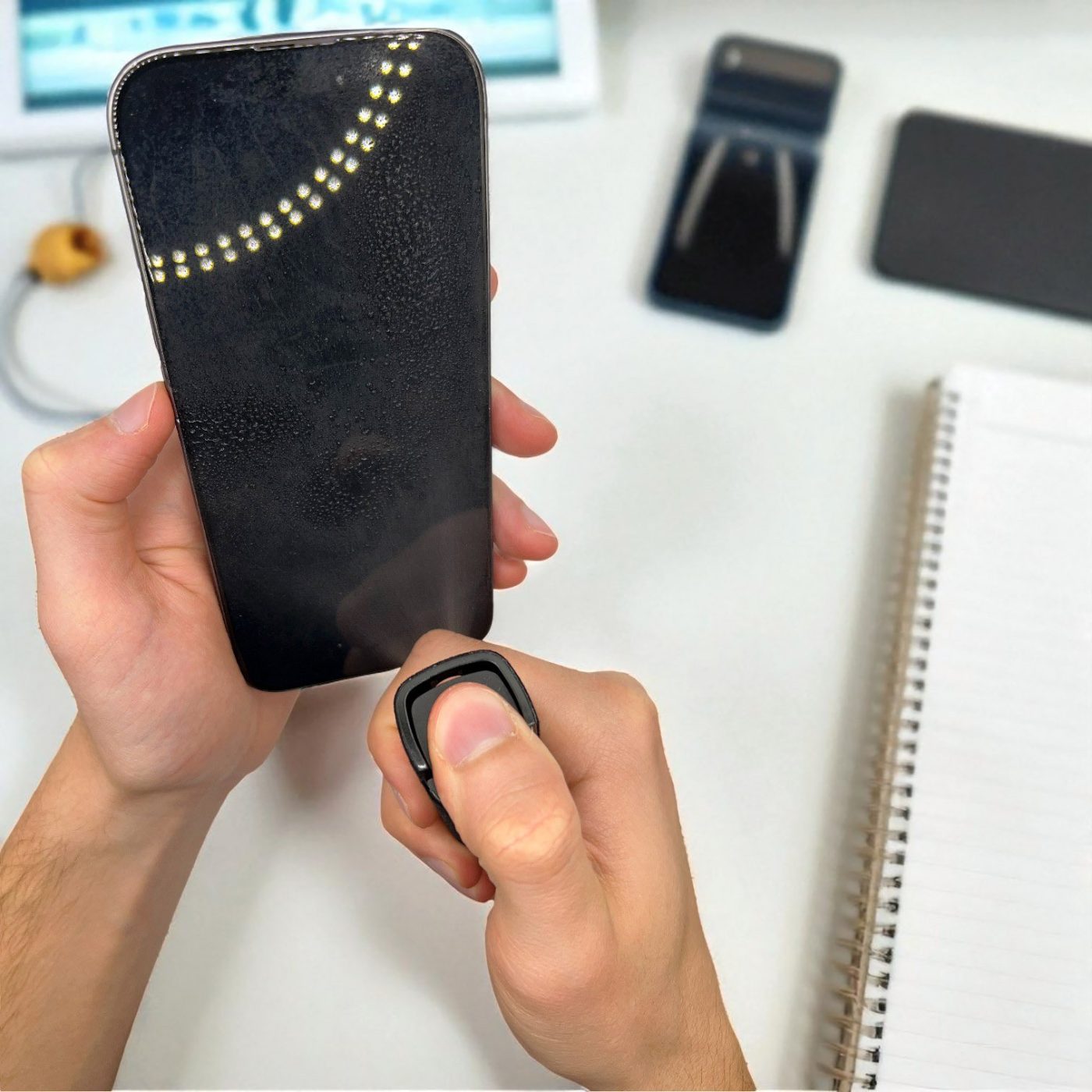Person using the screen cleaner spray on a phone with turned off display in a home office desk setting.