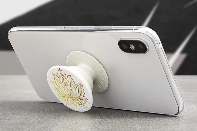 PopGrip with custom design White phone with a gold floral PopSocket attached, proped like a stand on a flat surface.