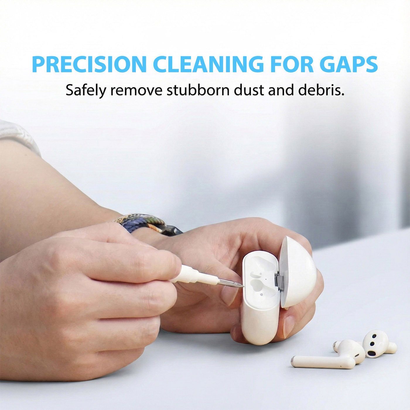 Hands using metal precision nib of cleaning tool to remove debris from crevices in a white wireless charging case.