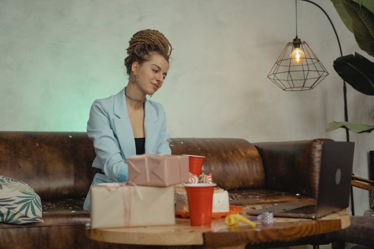 Woman sitting on a couch opening gifts after her birthday while using her laptop.